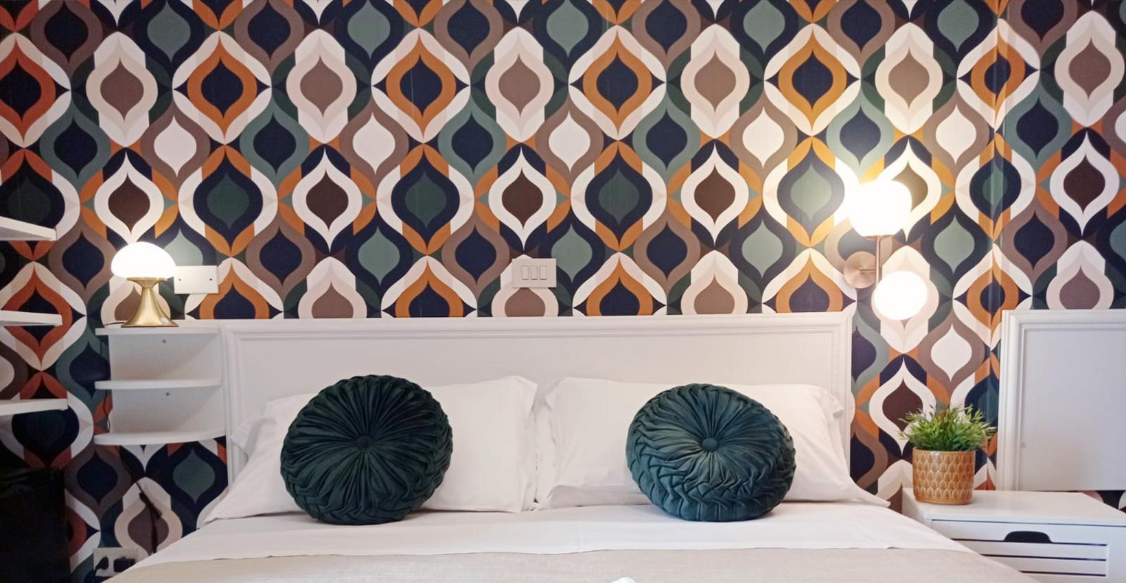 Camera da letto con carta da parati geometrica e cuscini decorativi verdi.