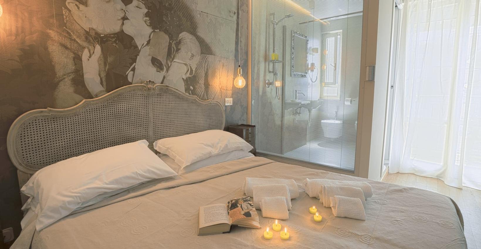 Camera romantica con letto matrimoniale, candele accese e bagno moderno a vista.