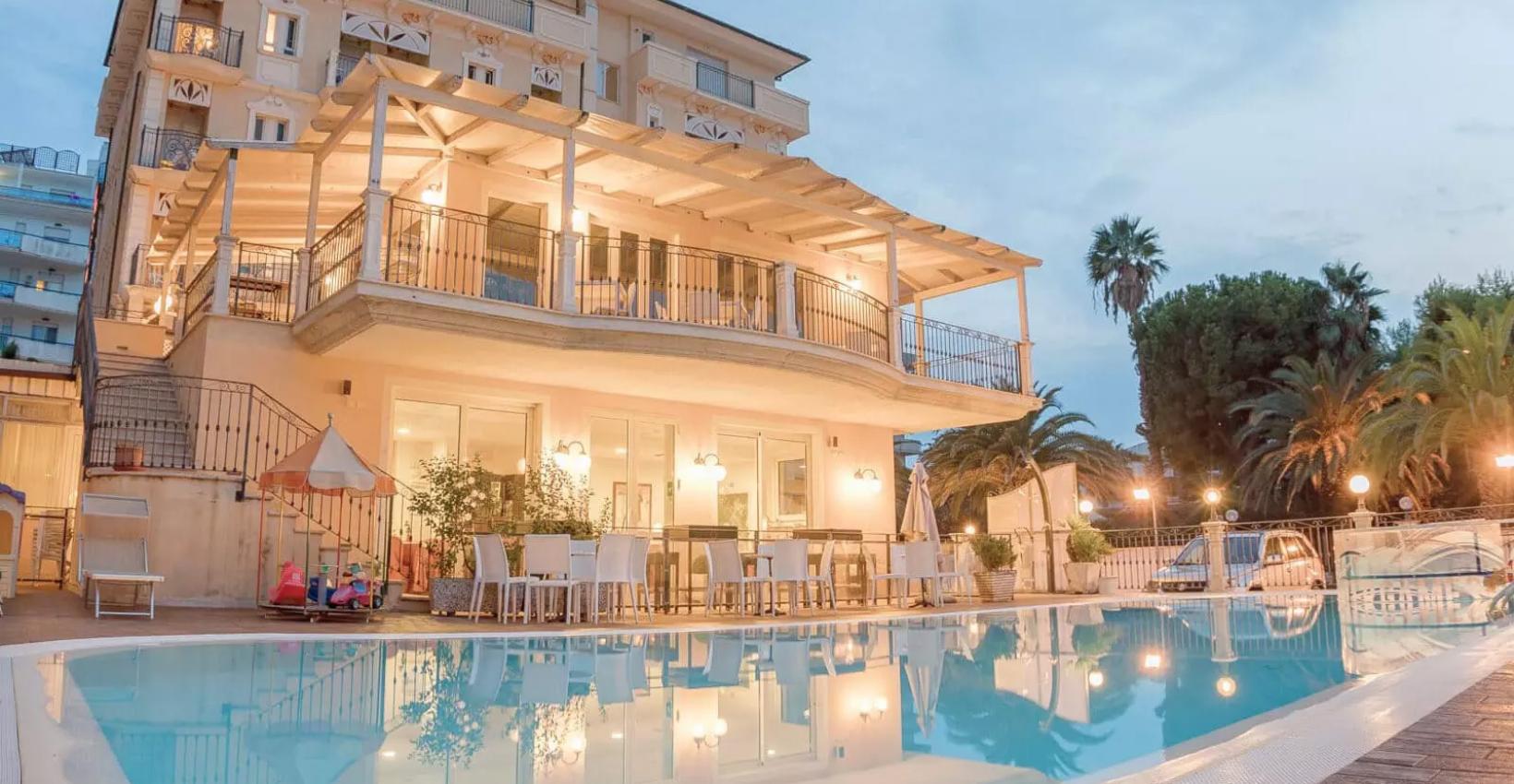 Villa elegante con piscina, terrazza illuminata e palme, atmosfera serale accogliente.