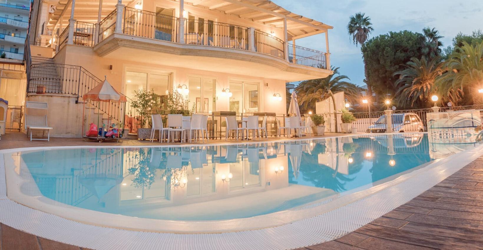 Elegante villa con piscina illuminata, circondata da palme, ideale per serate estive.