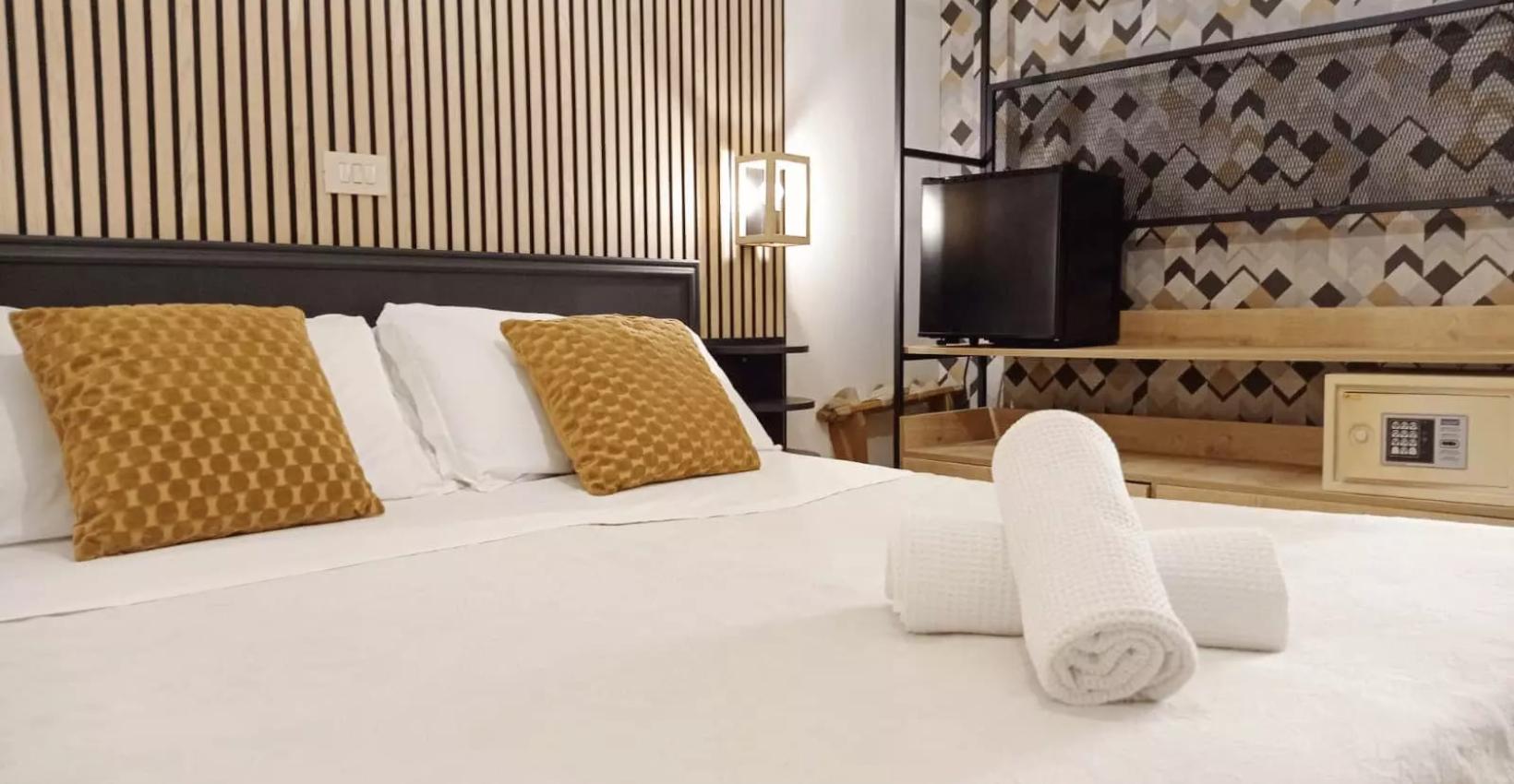 Camera moderna con letto matrimoniale, cuscini gialli e asciugamani bianchi arrotolati.