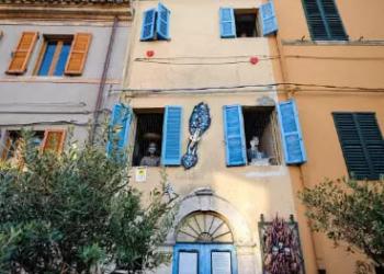 Facciata colorata con persiane blu e decorazioni, tra gli alberi.