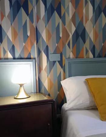 Camera da letto con carta da parati geometrica e lampada su comodino.