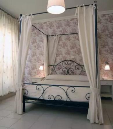 Camera da letto con letto a baldacchino, tende bianche e carta da parati floreale.