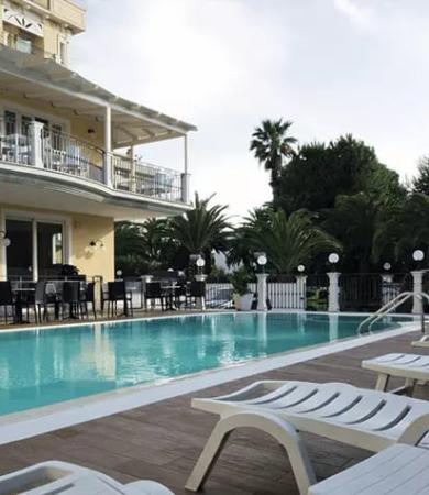 Piscina all'aperto con sdraio e palme, accanto a un edificio con balconi.