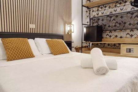 Camera moderna con letto matrimoniale, cuscini gialli, asciugamani, TV e cassaforte.