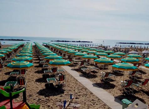 Spiaggia con ombrelloni verdi e gialli allineati, vista sul mare calmo.