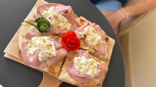Pizza con mortadella e crema, decorata con rose di verdure, su tagliere.