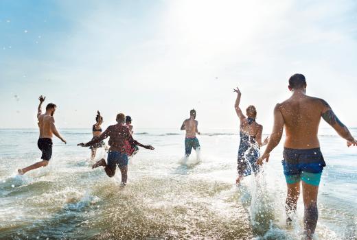 Gruppo di persone che si divertono correndo tra le onde del mare.