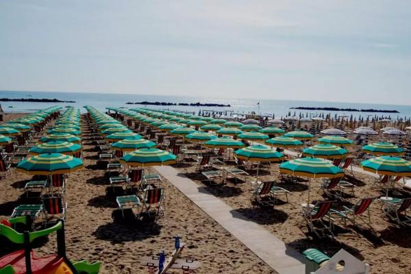 Spiaggia con file ordinate di ombrelloni e lettini colorati, vista mare.