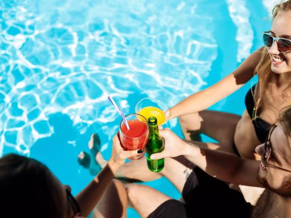 Amici brindano a bordo piscina con cocktail colorati sotto il sole estivo.