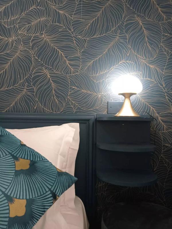 Camera elegante con carta da parati a foglie e lampada moderna su comodino.