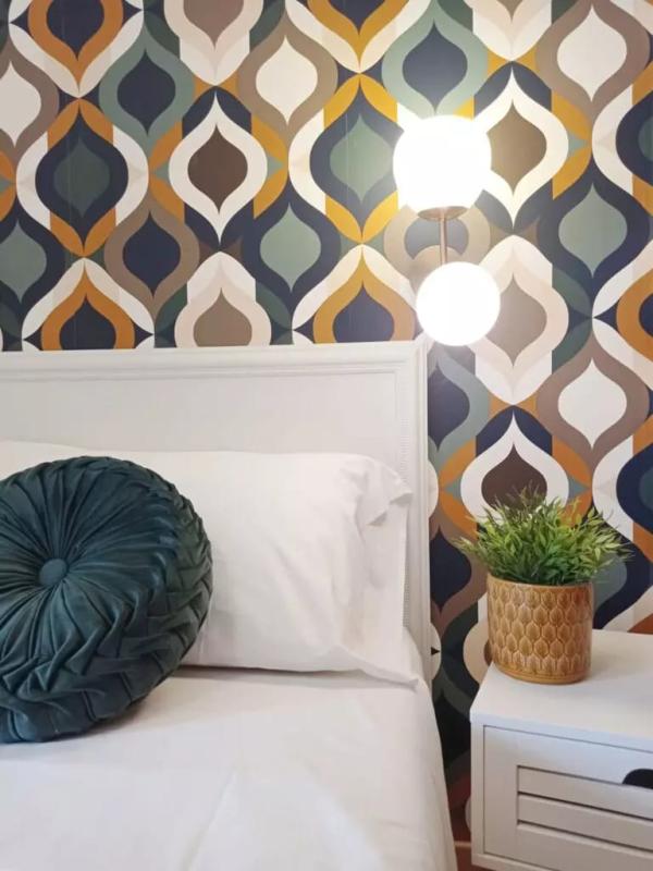 Camera da letto con carta da parati geometrica, lampada, cuscino verde e pianta.