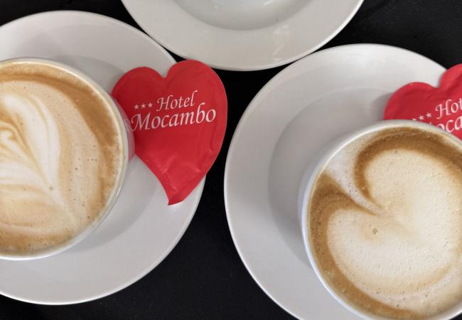 Tre cappuccini cremosi con bustine rosse a forma di cuore, atmosfera accogliente.
