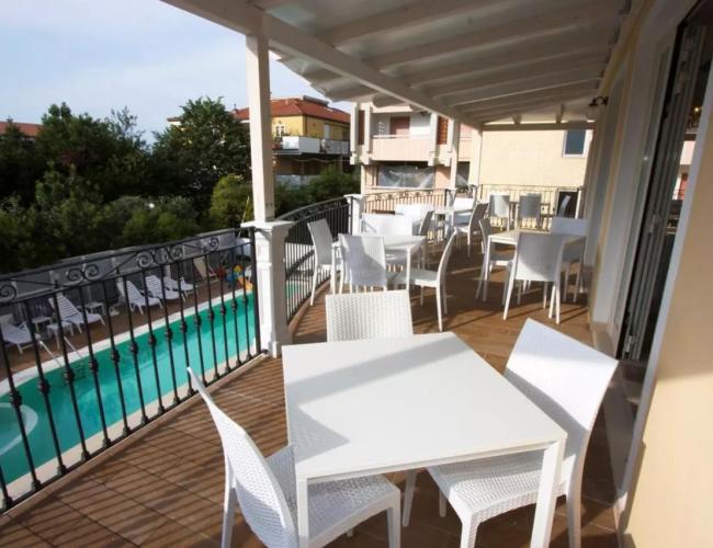 Terrazza con tavoli bianchi, vista sulla piscina e giardino circostante.