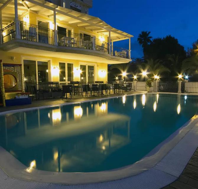 Villa illuminata con piscina riflettente, ambiente sereno e accogliente di notte.