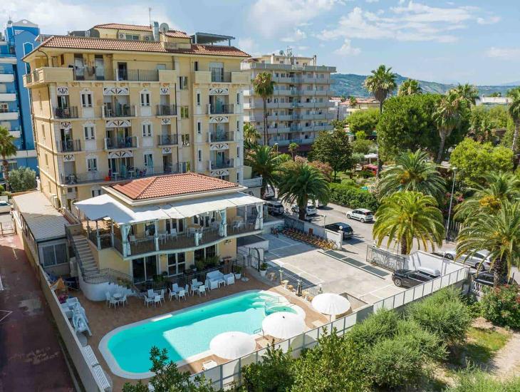 Hotel con piscina, terrazza e palme, situato in una zona verde e soleggiata.