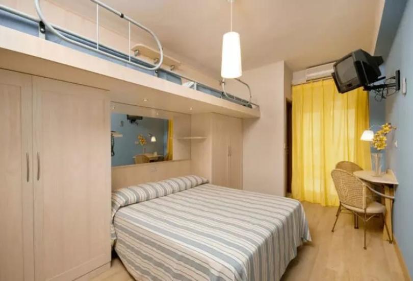 Camera da letto con letto a soppalco, scrivania, TV e tende gialle.
