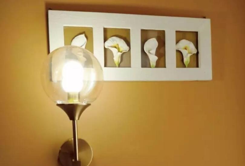 Lampada a muro con cornice di fiori bianchi su parete gialla.
