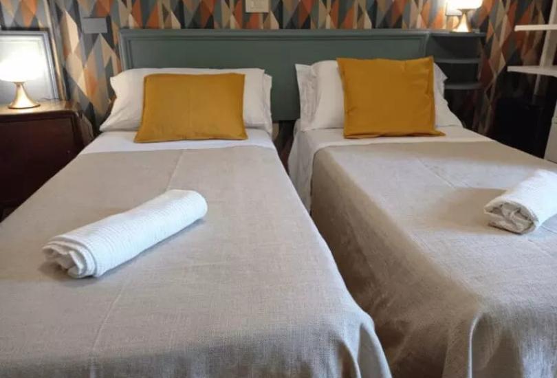 Due letti singoli con cuscini gialli e asciugamani su copriletto beige.