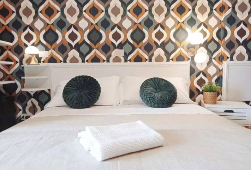Camera da letto con carta da parati geometrica, cuscini verdi e asciugamani bianchi.