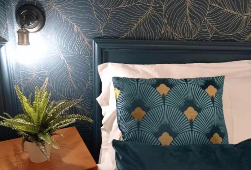 Camera da letto elegante con cuscini blu e carta da parati a foglie dorate.