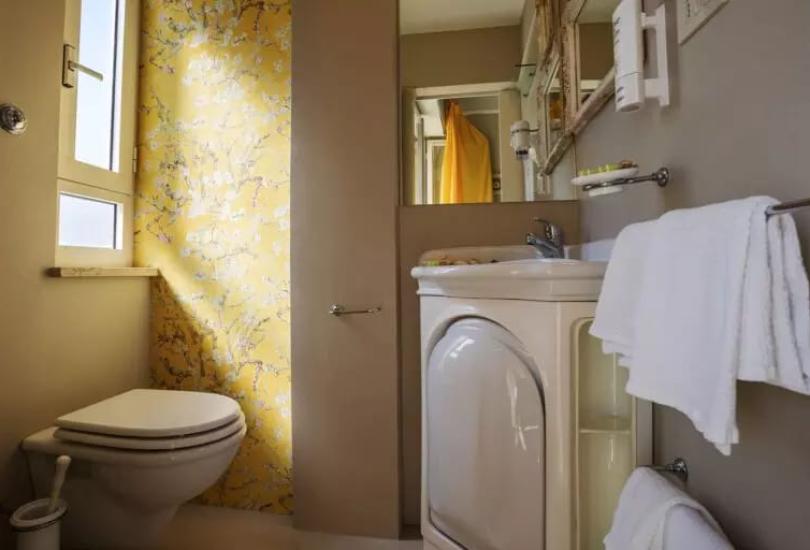Bagno con carta da parati gialla, wc e lavabo con specchio.