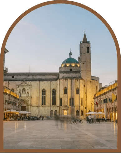 Piazza storica con cattedrale e torre, atmosfera serale e gente passeggia.